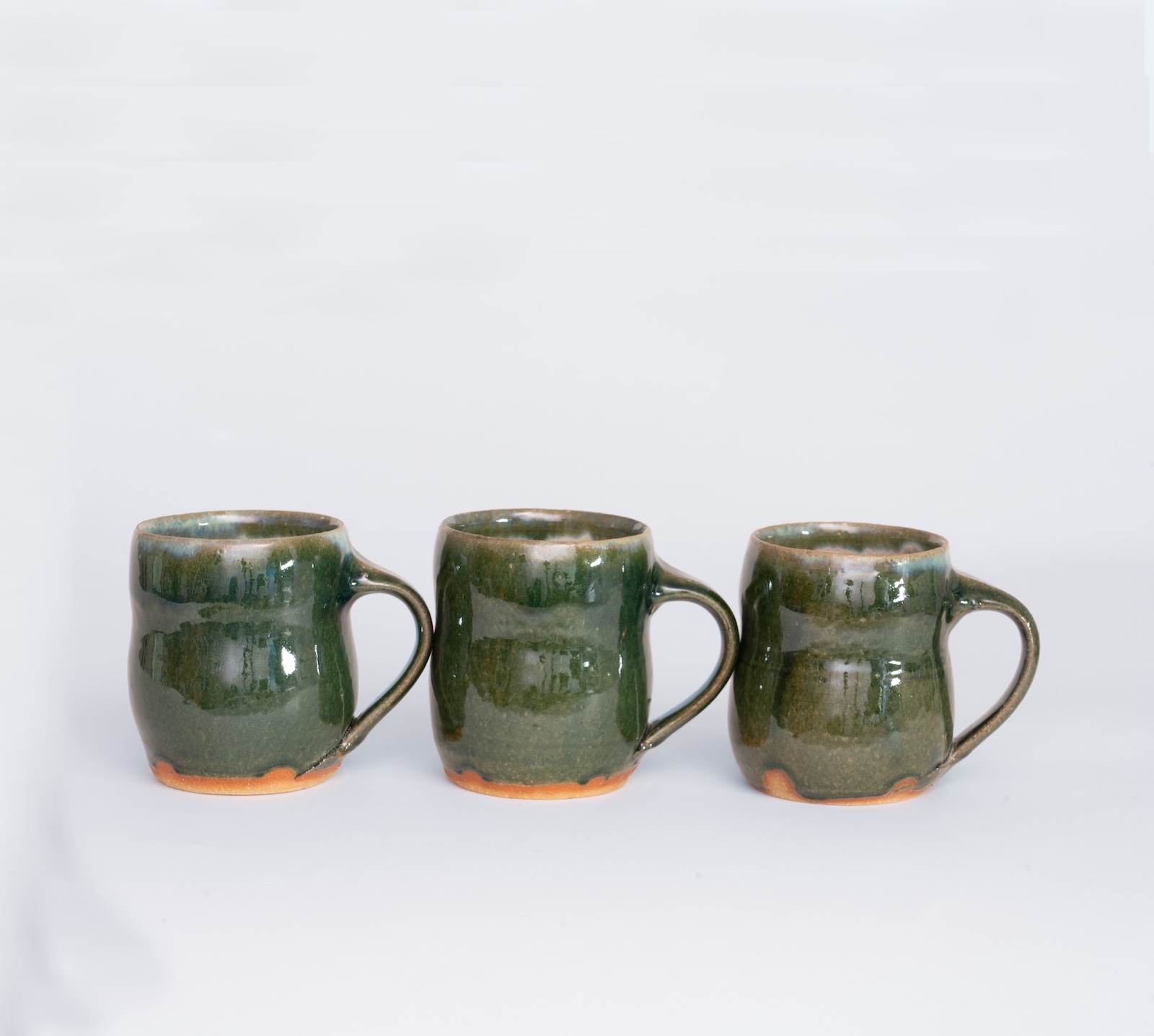 three large mugs next to each other. They are glazed glassy green