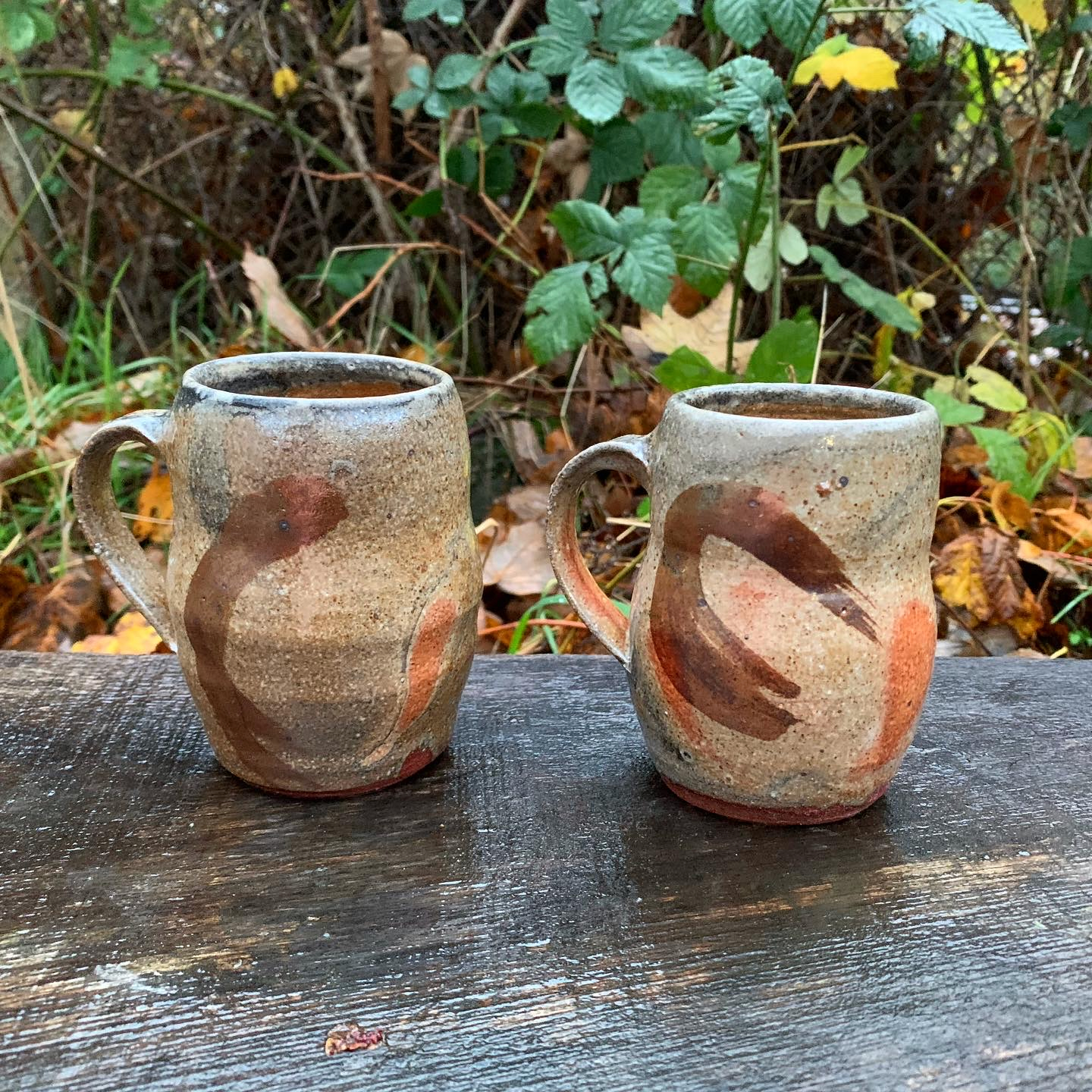 two mugs in a brownish golden glaze. The mugs are slightly cinched 
          at the middle and rounded above and below