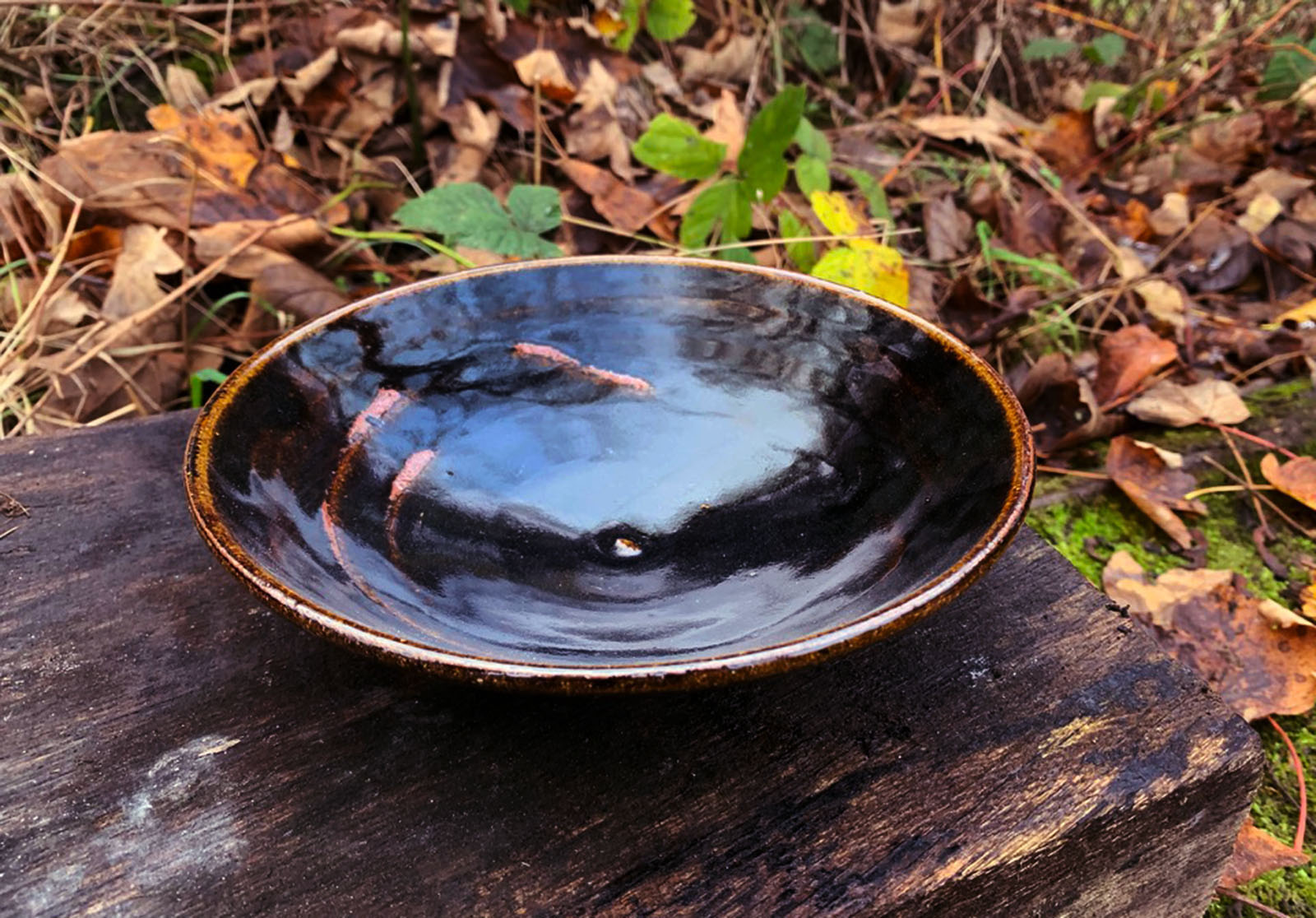 a shallow, wide bowl with a glossy black glaze that has two lines in lighter brown circling wavily through the bowl's inside