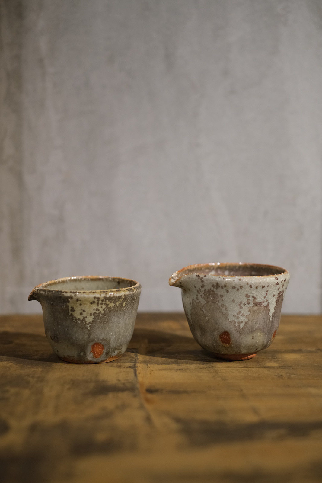 two greenish-grey gongdaobei with red fingermarks showing through 
          at the bottom of the glaze. They have wide tops and taper to a simple rounded foot.