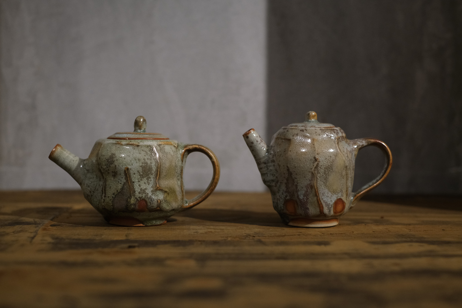 two teapots with somewhat wavy
        beveled sides. They are glazed in a matte, greenish grey glaze.