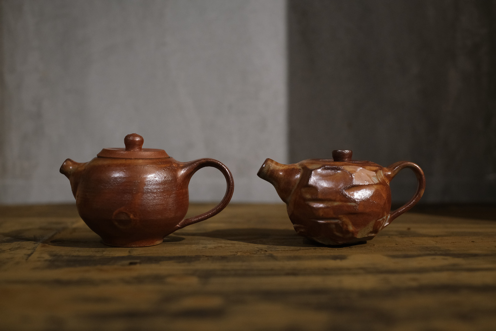 two round bellied teapots in a matte brownish-red glaze. One has carved edges, the other is smooth