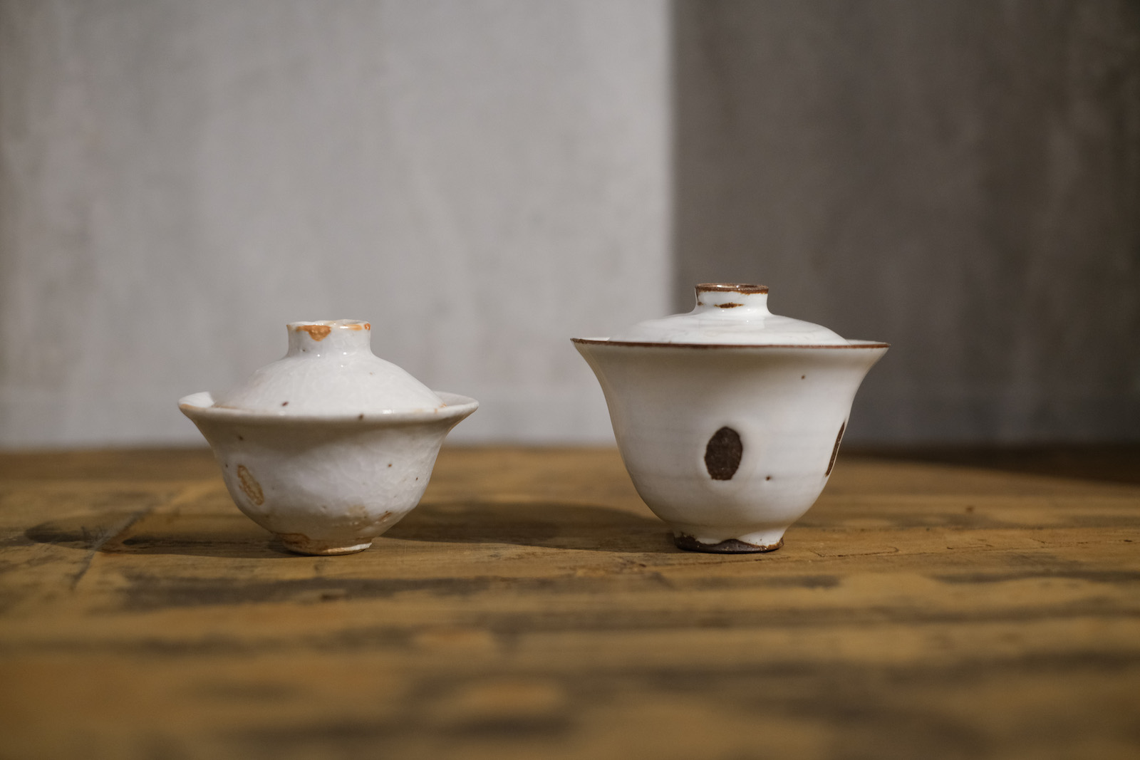 two rustic looking gaiwan in a white glaze. Under an unglazed 
          part of one of the two, the dark purple clay body is visible.