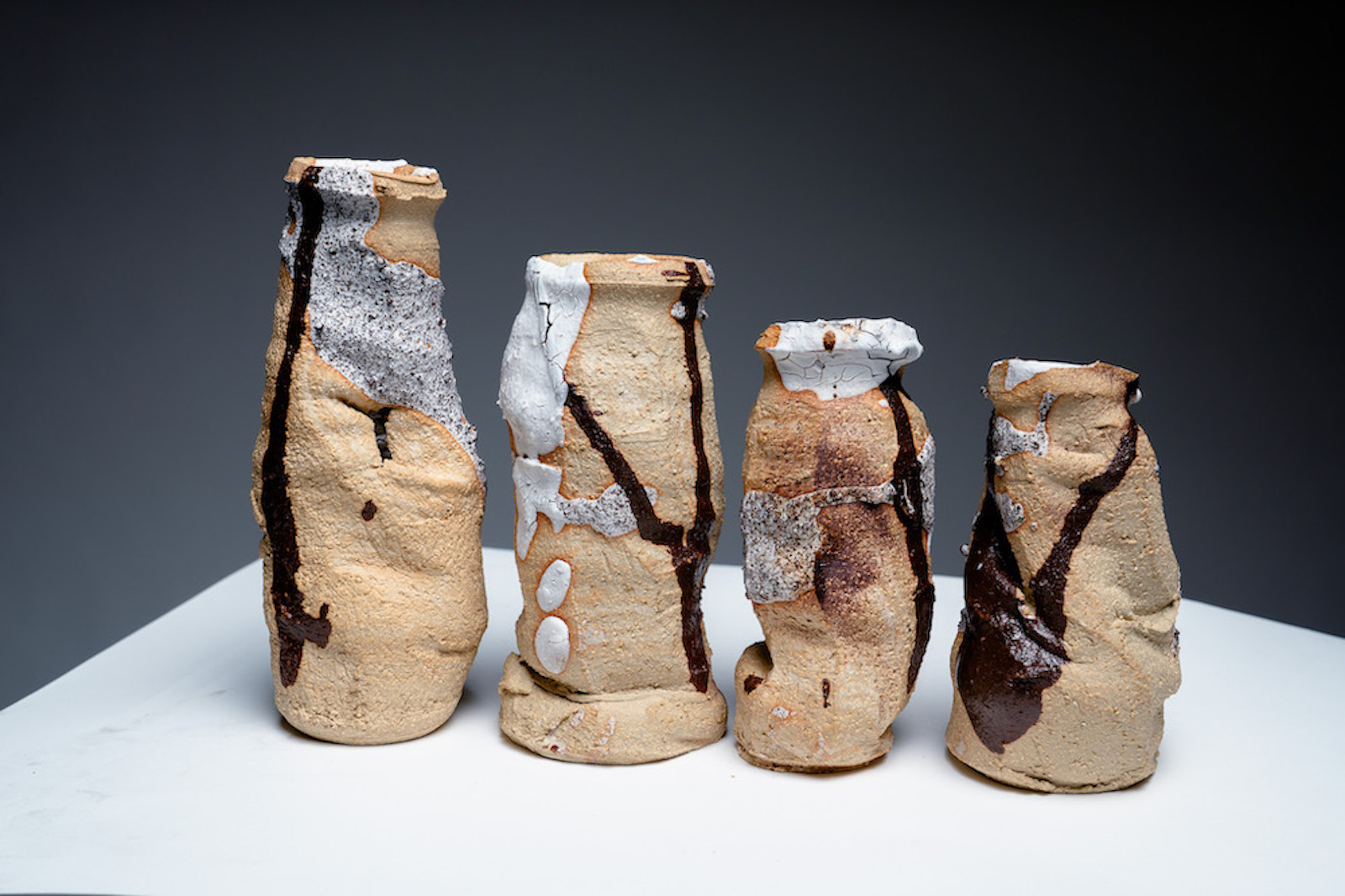 four tall, thin vases all looking somewhat collapsed. Unevenly covered in earthy maroon and white glaze