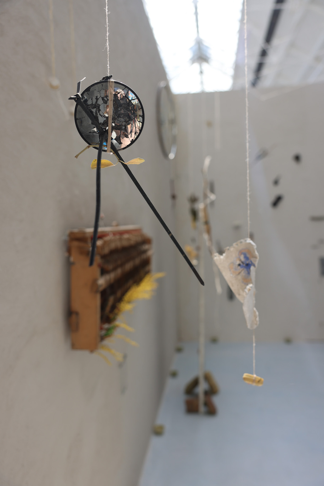 one of the small hanging sculptures. In this case, a broken
        bycicle side-mirror suspended from a pinkish-cream thread with a zip tie and a yellowed seedling wrapped into it.