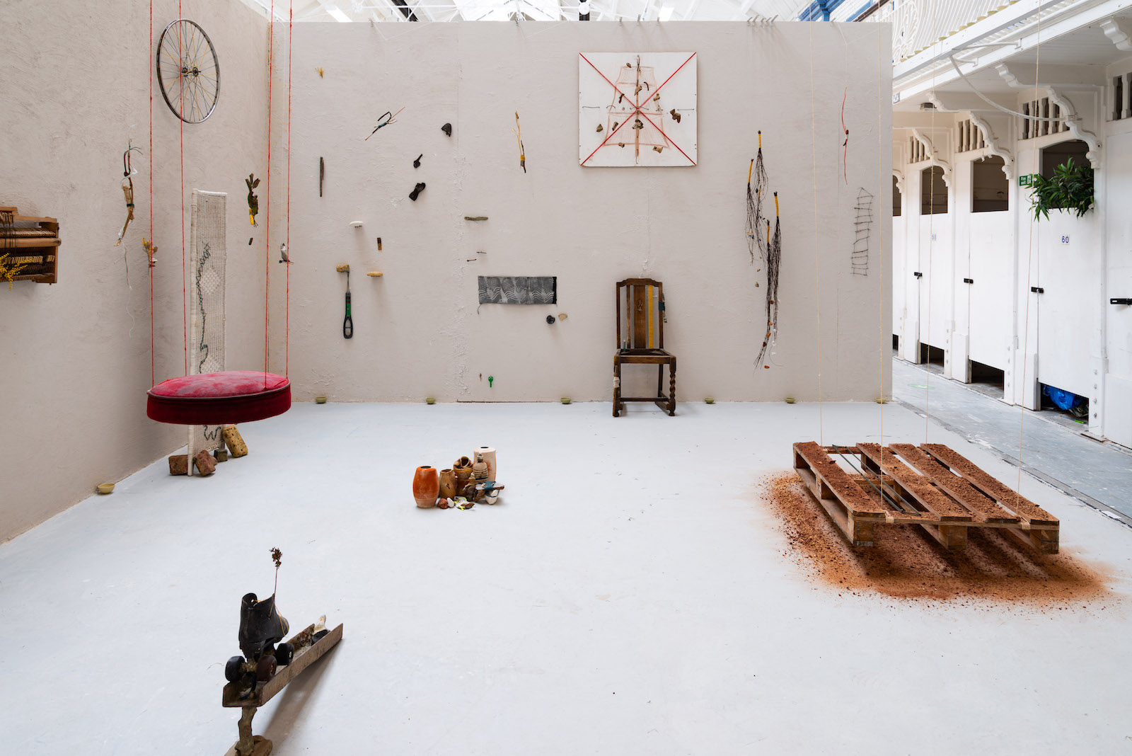 a wall covered in clay 
        with various artworks suspended from string infront of it