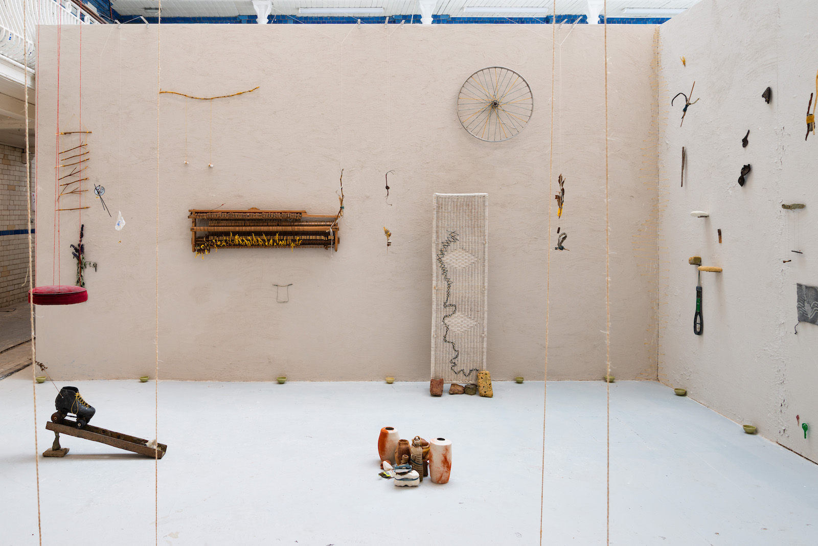 a wall covered in clay 
    with various artworks suspended from string infront of it