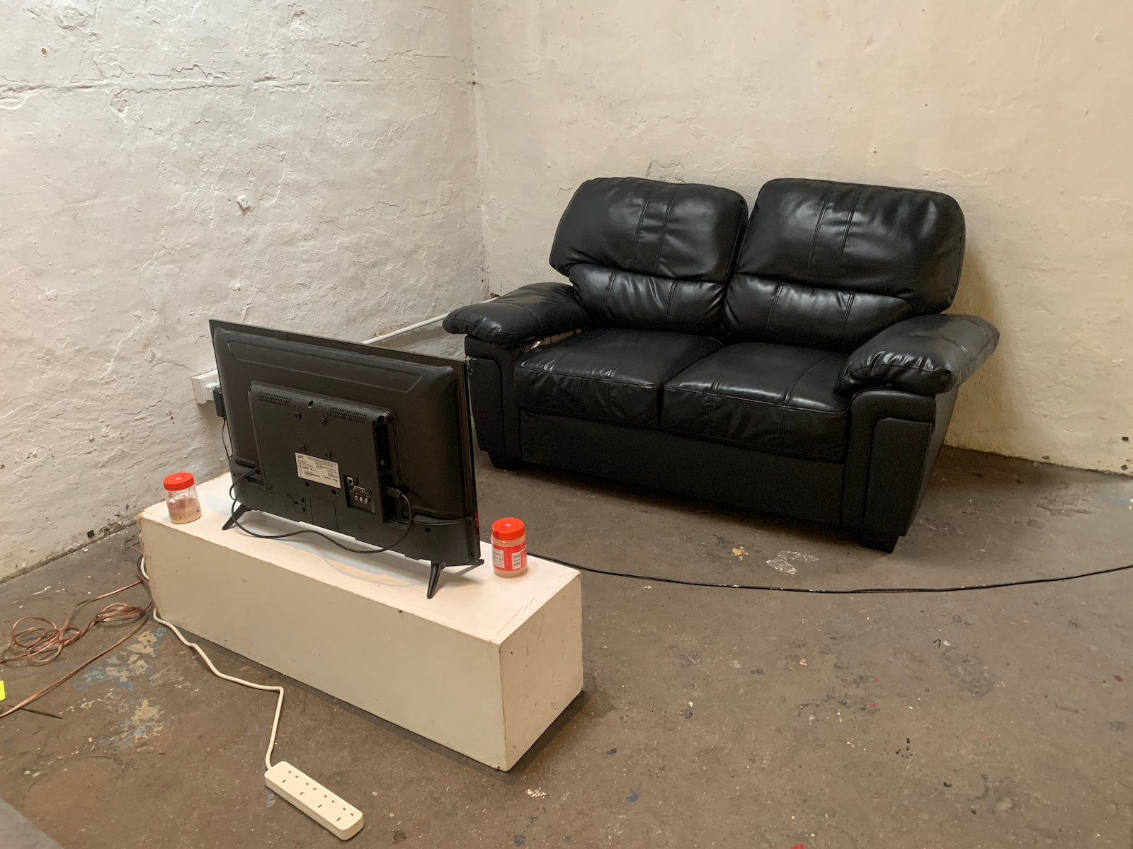 a two-seater leather couch facing a tv in the corner of a room 
            with white painted brick walls and a cement floor.