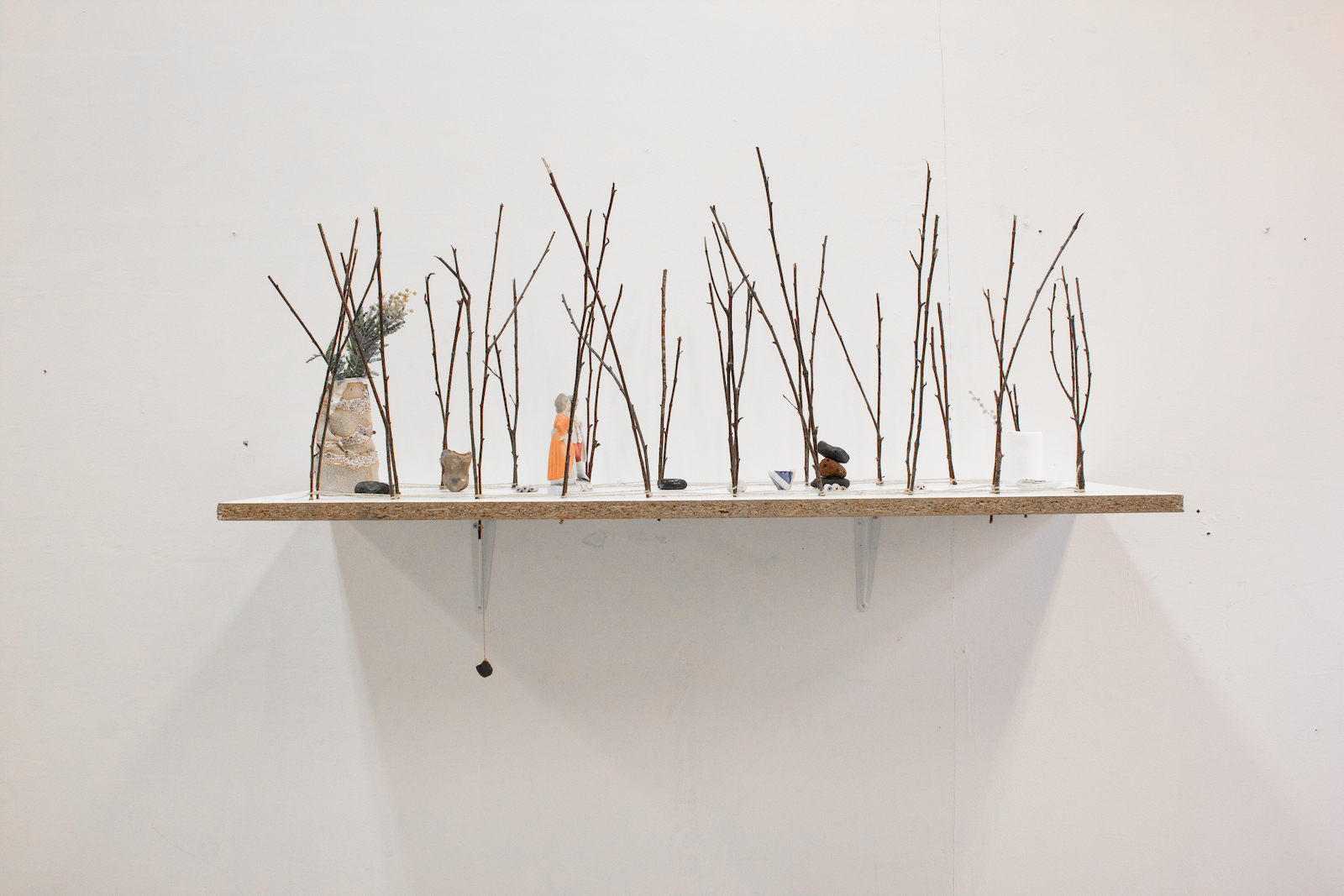 a horizontal board with ceramic figures, walking between a double line of trees modeled by small twigs.