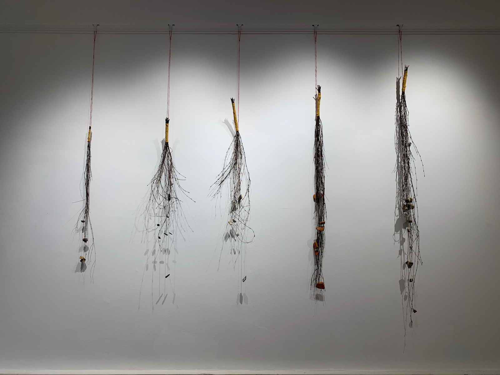 bundles of birch twigs suspended from thread
         against a wall with bits of soil, clay, and other materials tied into the sticks