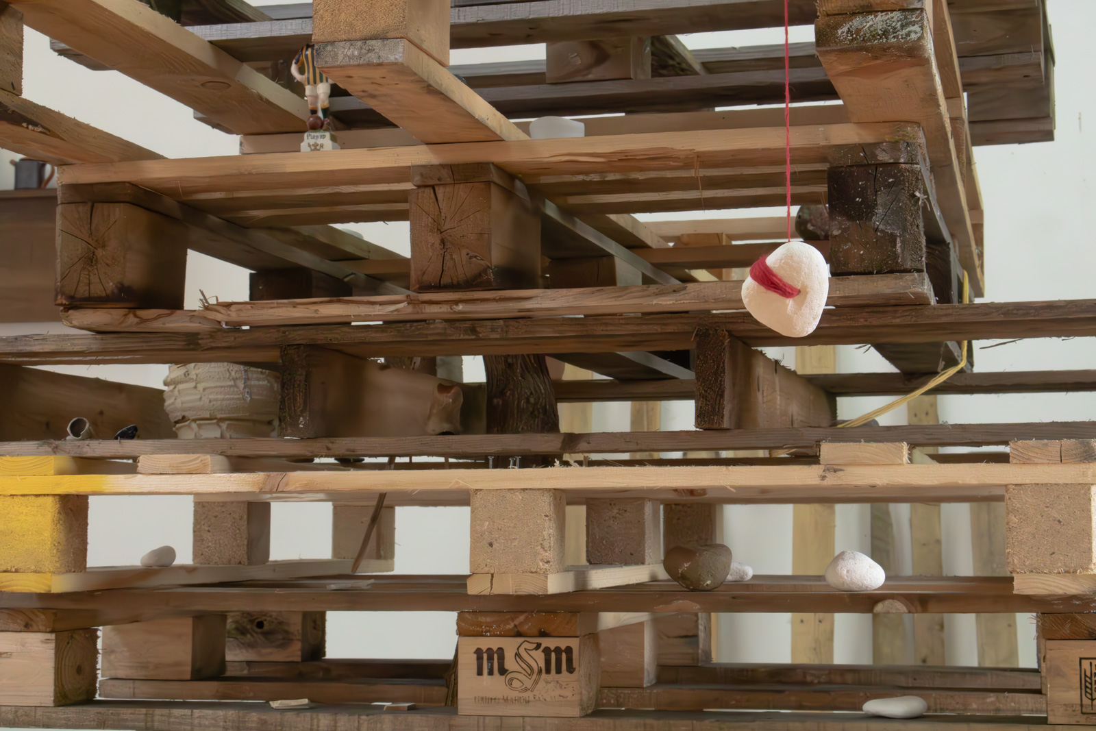 a piece of chalk with a whole through it, suspended in 
        the air by a red thread tied to an overhanging pallet.