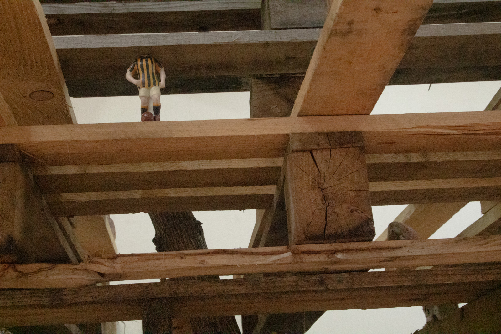 a view of an old sports trophy showing a boy with his 
        foot on a socer ball. The trophy is between two levels of 
        pallets and its head is missing or embeded into the pallet above.