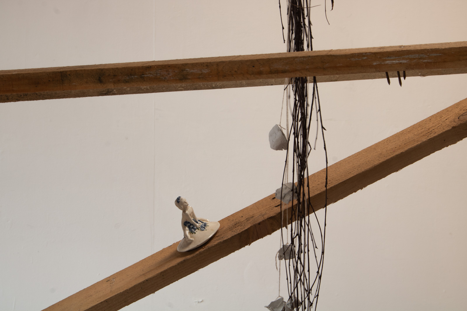 a closer view in which the blue and whit ceramic child is seen behind the 
        bundle of birch twigs. The clay suspended in the birch twigs is very white