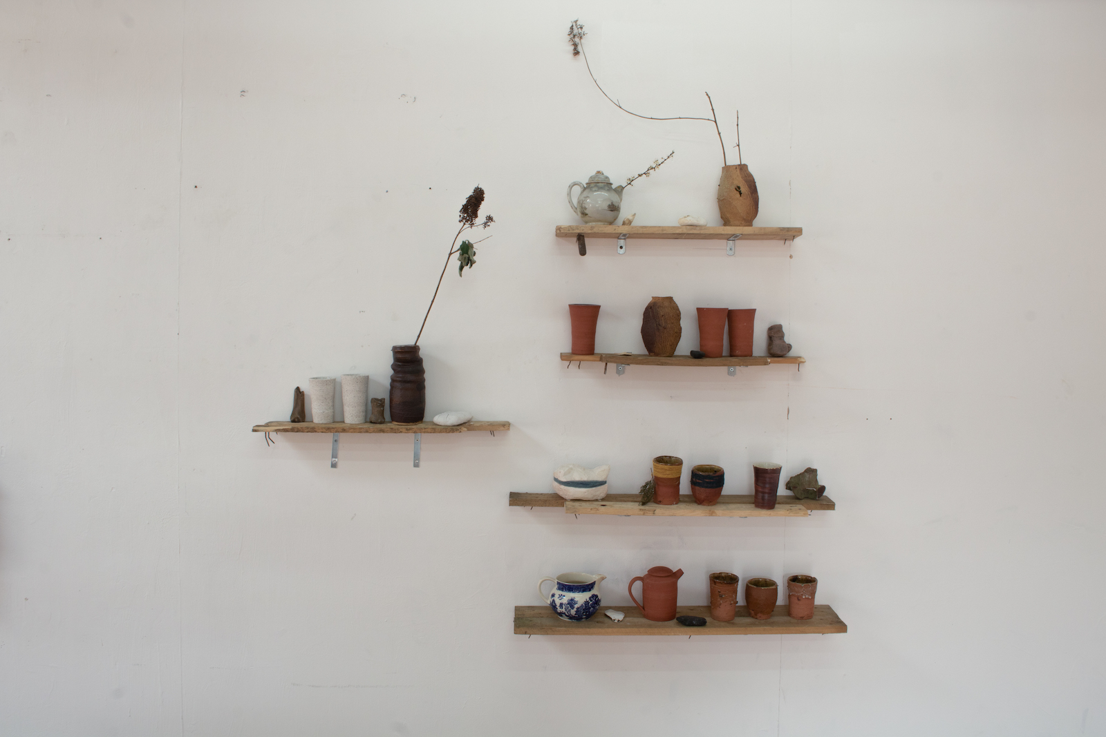 boards on a wall with small ceramic 
        sculptures on them. Some of the sculptures are old ceramic pieces that look like they 
        are antiques, others are thrown pots made out of a dark clay